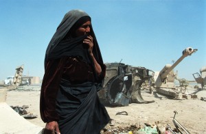 A woman stands in front of discarded military scrap in Iraq. 06/01/2003. Photo credit: Philip Reynaers/Greenpeace